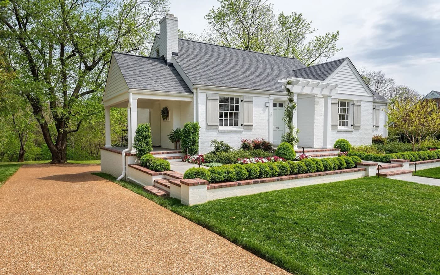 White brick Tennessee home with mature trees, landscaped gardens and a covered porch.
